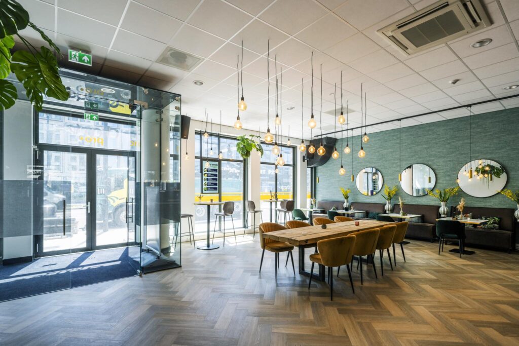 Modern lobby interior at Elizabeth Cady Stantonplein with large wooden tables, velvet chairs, pendant lighting, and floor-to-ceiling windows.
